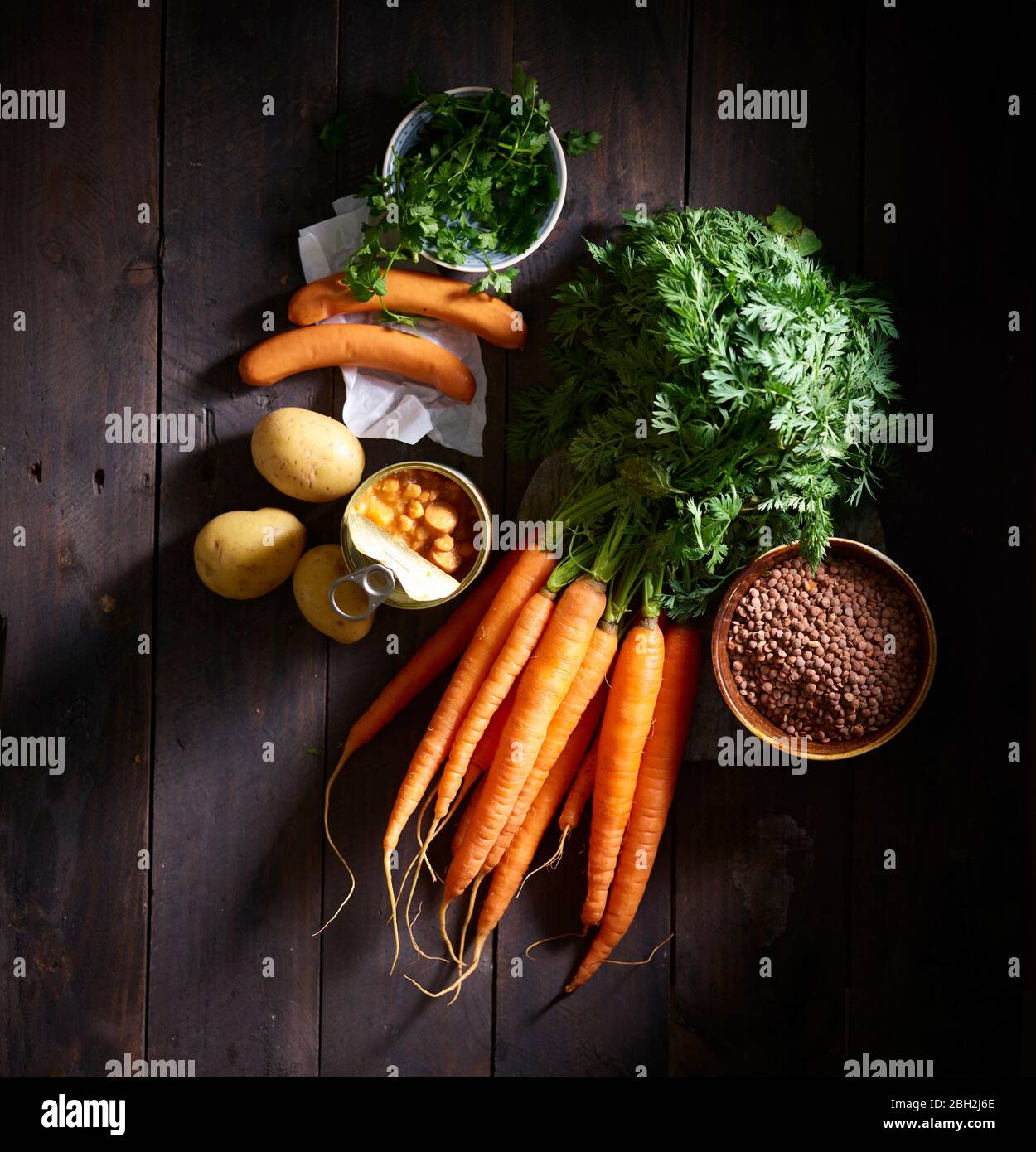 Ein Bündel Karotten, Würstchen, Petersilie, Kartoffeln, Linsensuppe aus der Dose und eine Schüssel Linsen Stockfoto