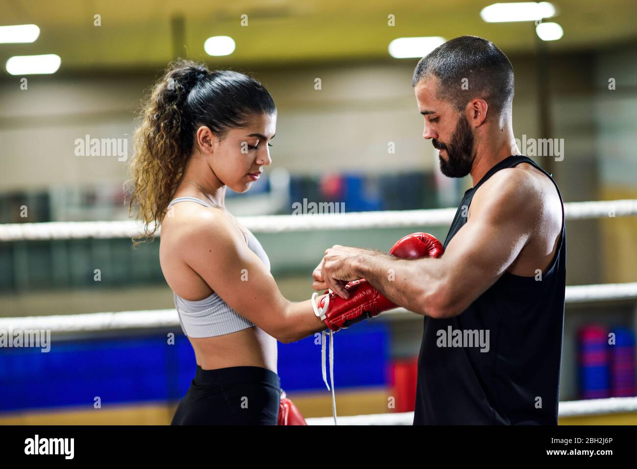 Trainer, der die Boxhandschuhe auf eine junge Boxerin legt Stockfoto