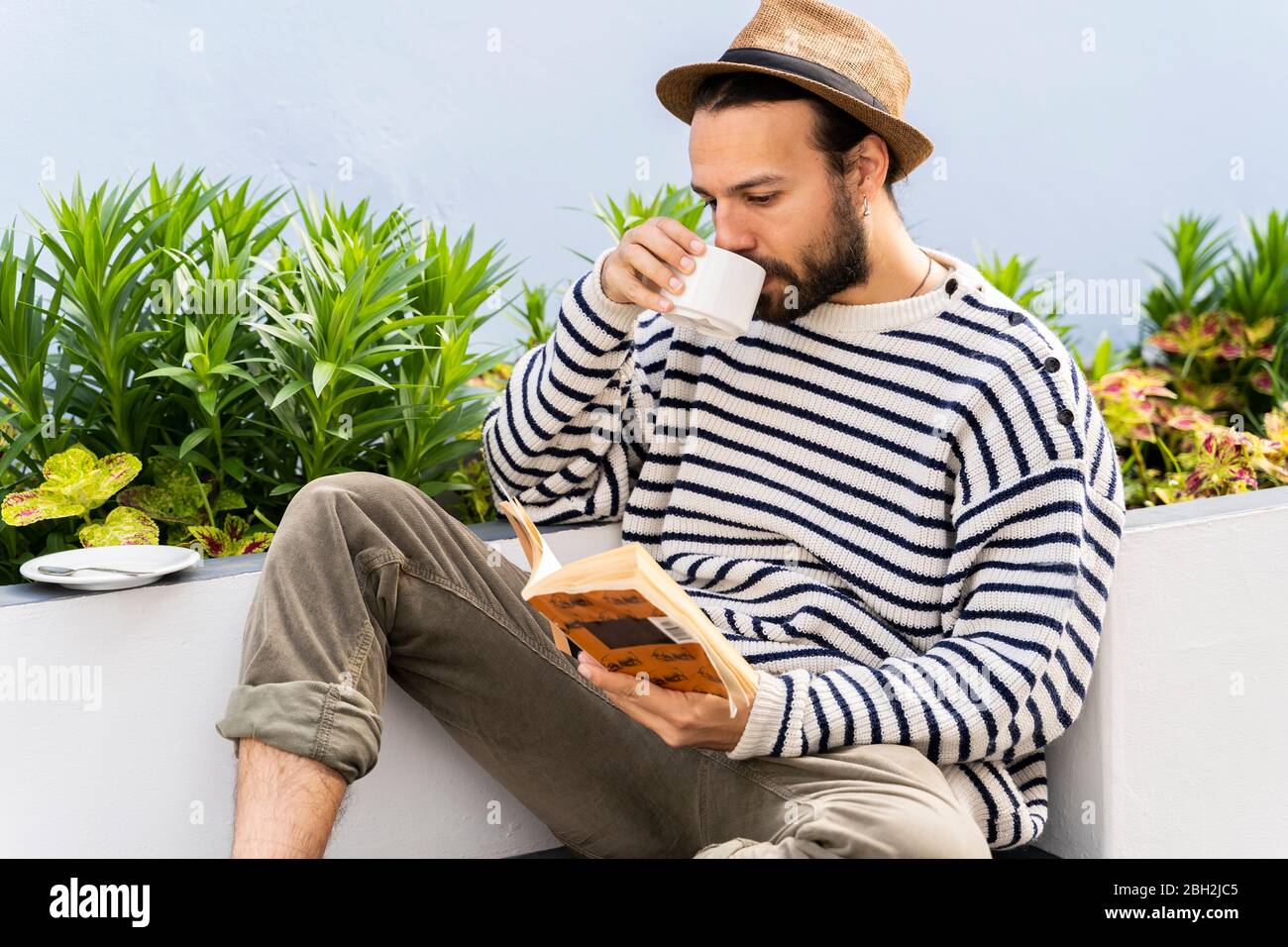 Mann, der auf dem Balkon saß, Kaffee trank und ein Buch las Stockfoto