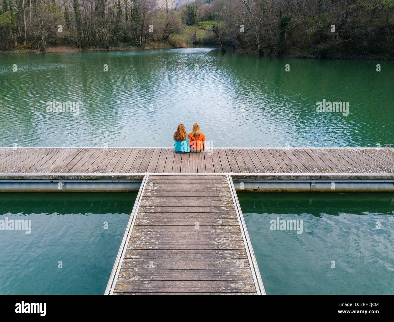 Rückansicht von zwei Freunden, die nebeneinander auf dem Steg, Valdemurio Reservoir, Asturien, Spanien sitzen Stockfoto