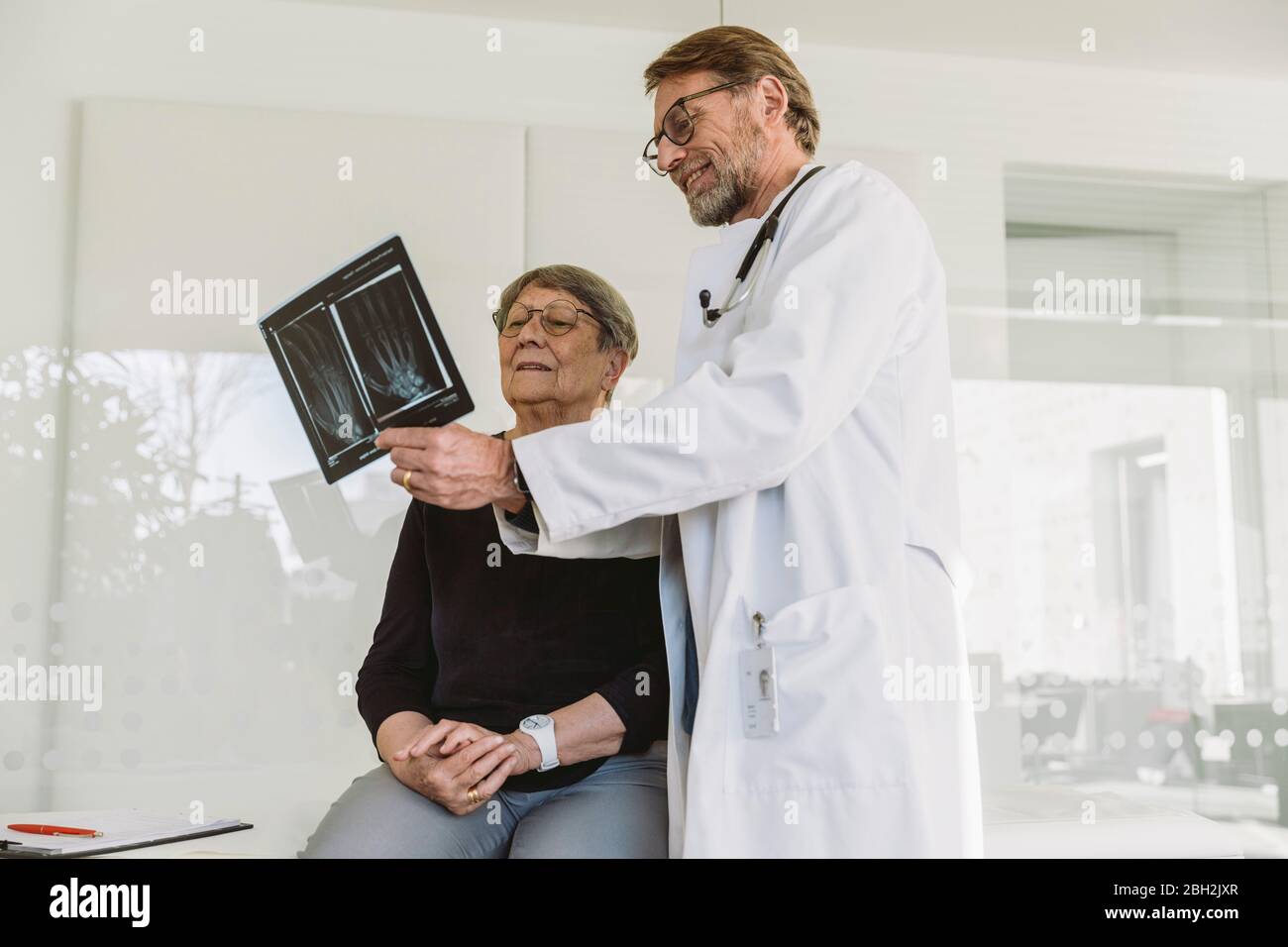 Arzt bespricht Röntgenbild der gebrochenen Hand mit dem älteren Patienten Stockfoto Arzt bespricht Röntgenbild der gebrochenen Hand mit dem älteren Patienten Stockfoto