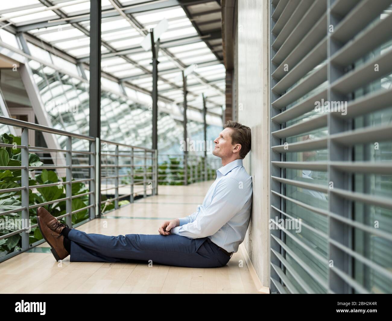 Geschäftsmann im grünen Atrium, auf der Galerie sitzend, denkend Stockfoto