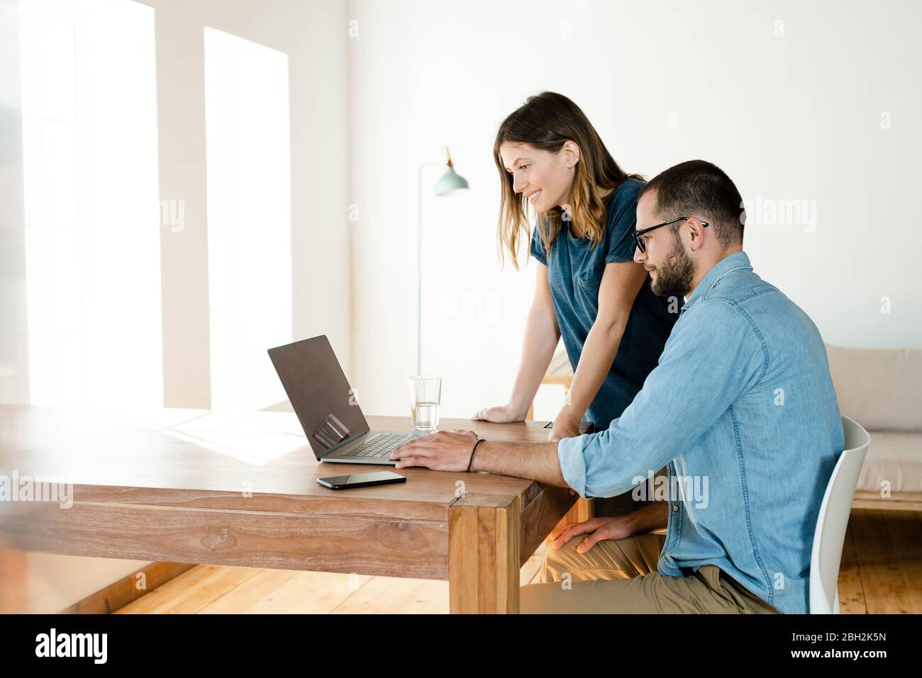 Lächelndes Paar, das von zu Hause aus im modernen Wohnzimmer am Laptop arbeitet Stockfoto