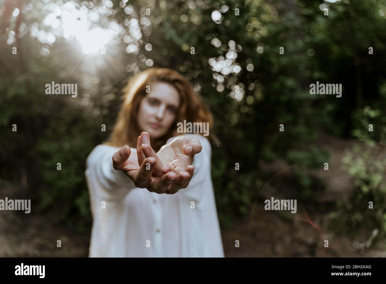 Junge rothaarige Frau streckt ihre Hände im Wald aus Stockfoto