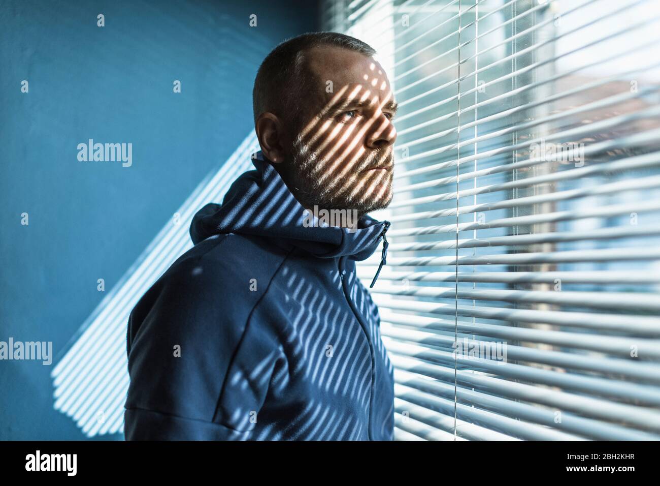 Nachdenklicher Mann, der aus dem fenster des venezianischen Jalousien schaute Stockfoto