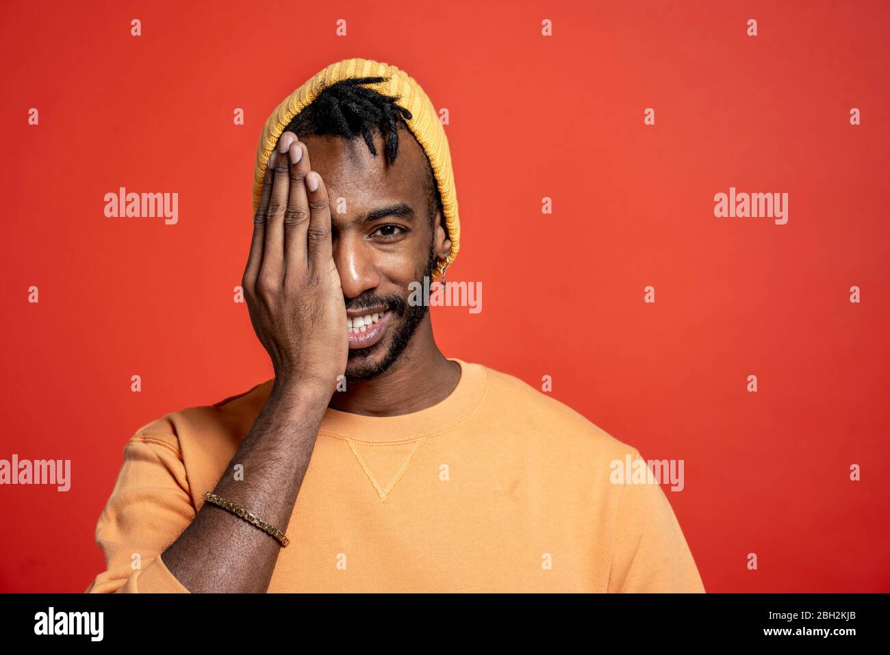 Porträt eines stilvollen jungen Mannes mit einem Auge vor der orangen Wand Stockfoto