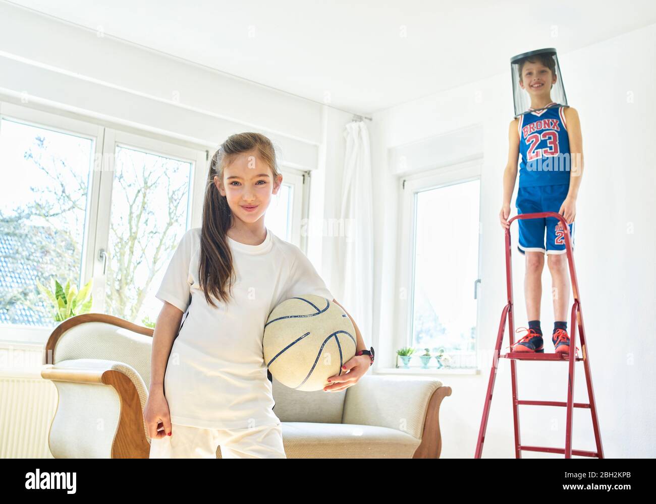 Portrait von Mädchen und Jungen Basketball spielen im Wohnzimmer Stockfoto