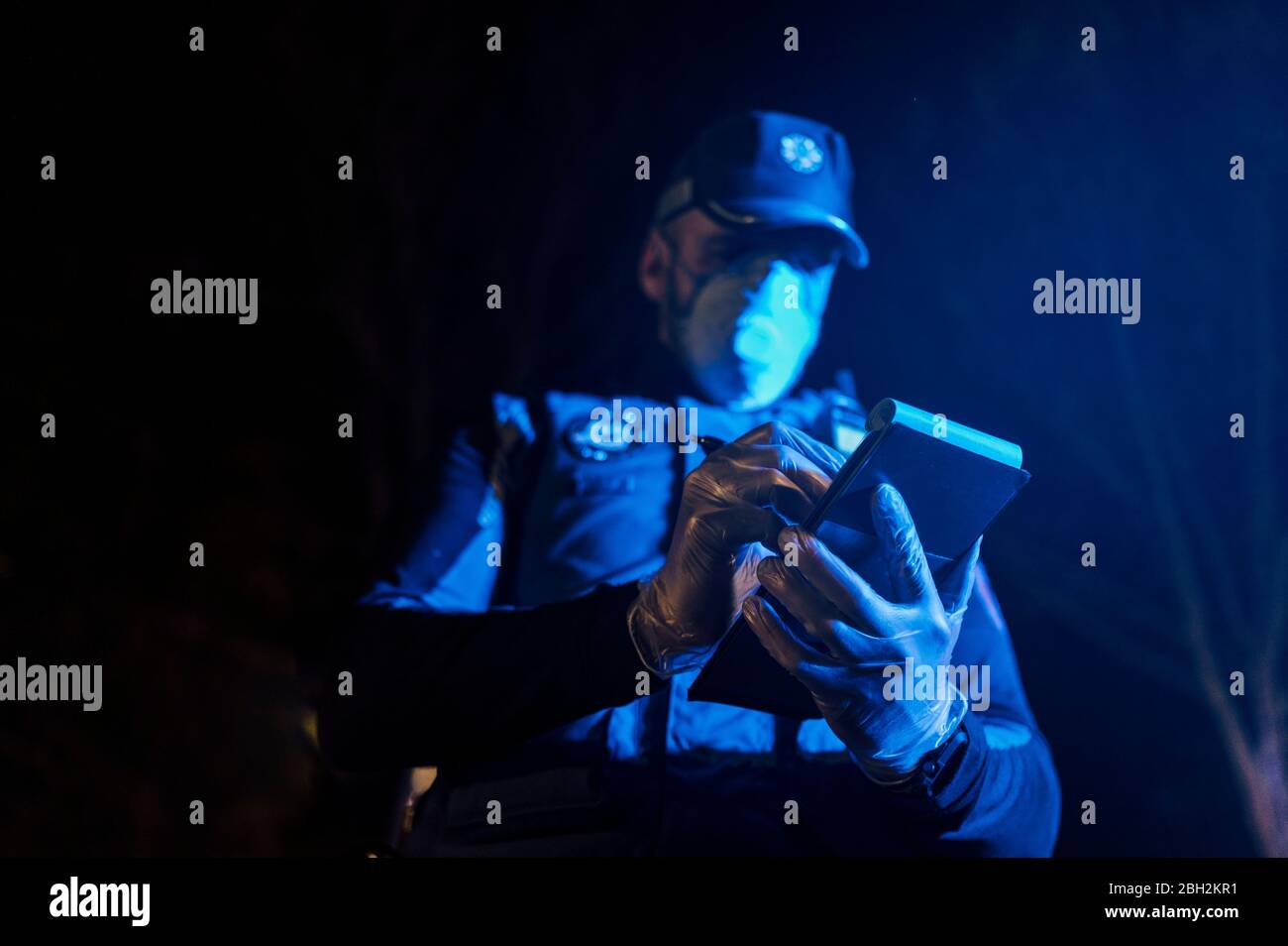 Polizist während der Notmission in der Nacht, Notizen, Schutzhandschuhe und Maske tragen Stockfoto