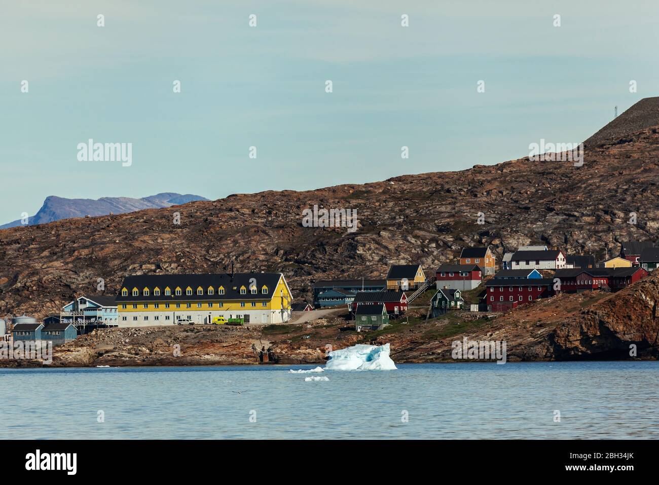 Traditionelle Häuser in Upernavik Bucht mit einem großen gelben öffentlichen Gebäude, mit Eisberg im Vordergrund Stockfoto