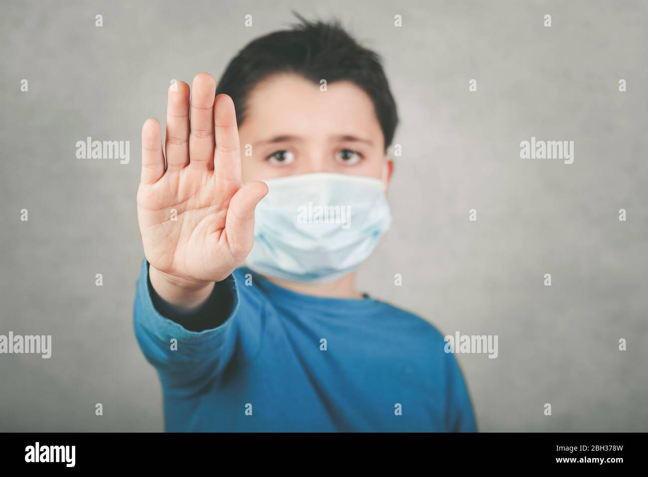 Stop Coronavirus, Kind trägt medizinische Maske zeigt ein Stoppschild über grauen Hintergrund, Hintergrund Unschärfe Stockfoto