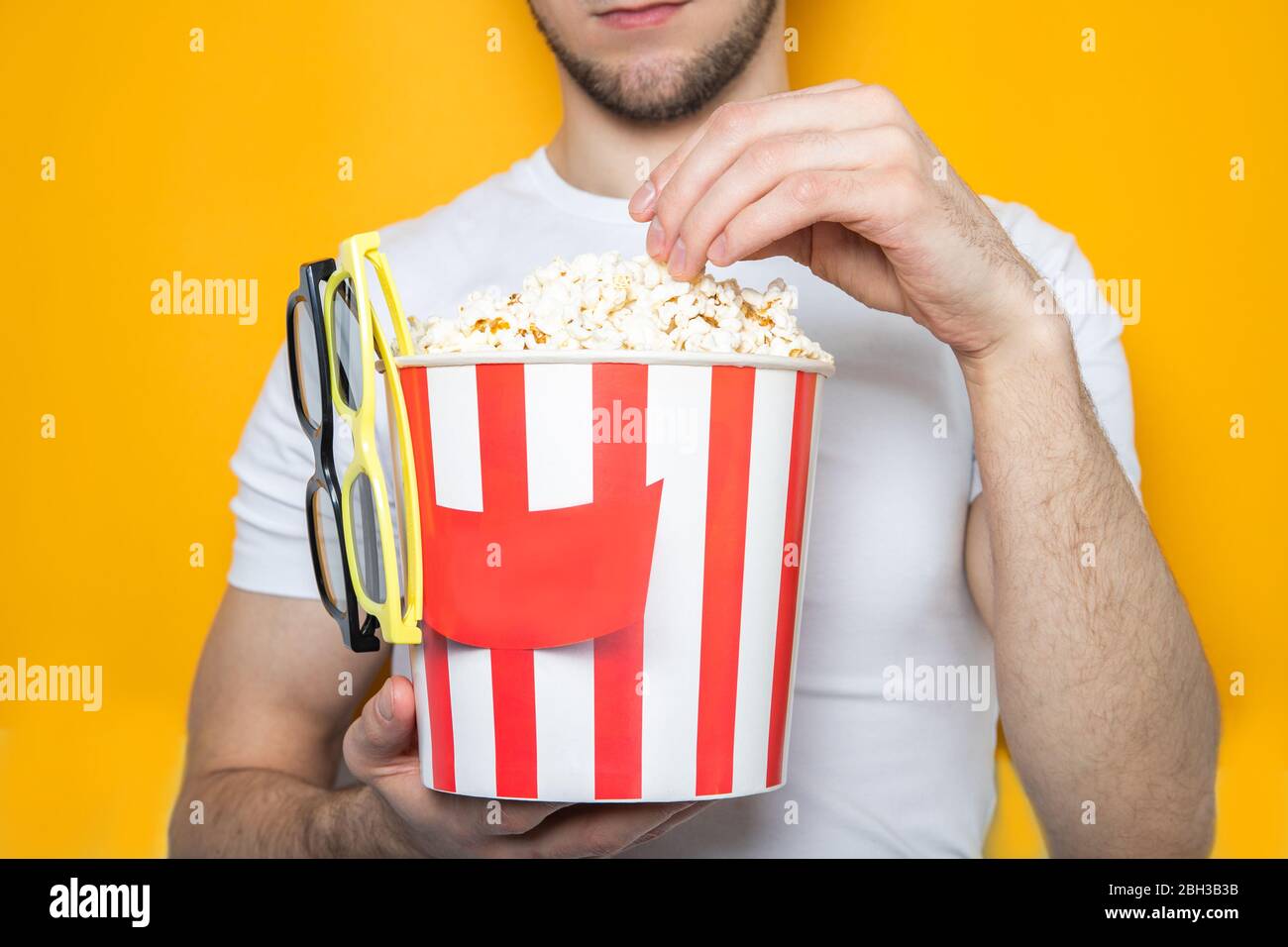 Schöner Kerl hält Popcorn und 3D-Brille. Gelber Hintergrund. Nahaufnahme Stockfoto