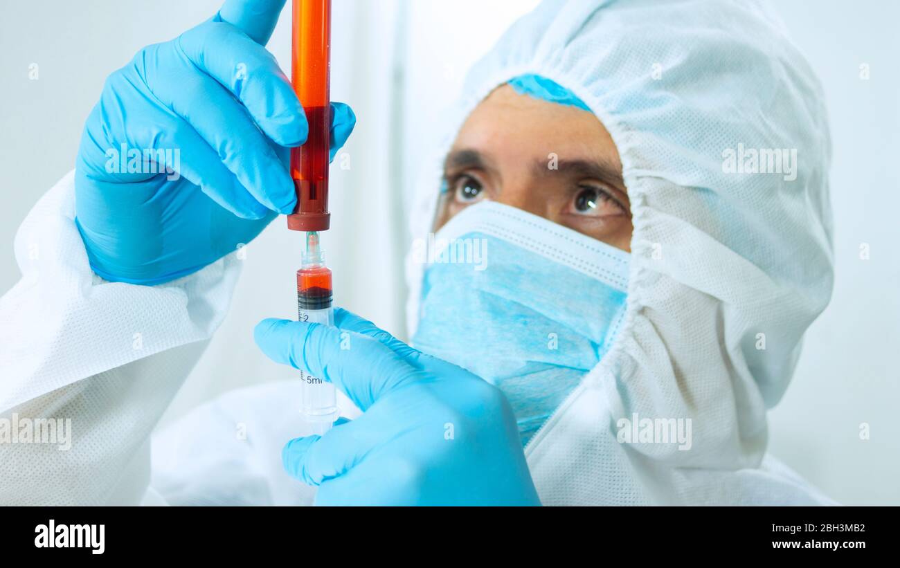 Nahaufnahme des latein-Arztes in Bioprotective-Anzug, Gesichtsmaske und blauen Handschuhen, die eine Blutprobe in einem Reagenzglas mit einer Spritze auf weißem Hintergrund entnehmen Stockfoto