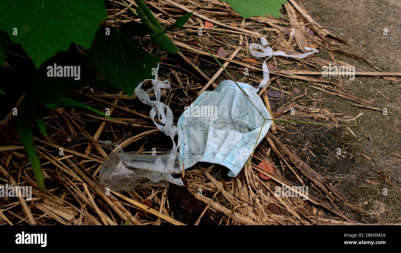 Nahaufnahme der gebrauchten blauen Tuch Gesichtsmaske auf der Straße zwischen den Müll geworfen Stockfoto
