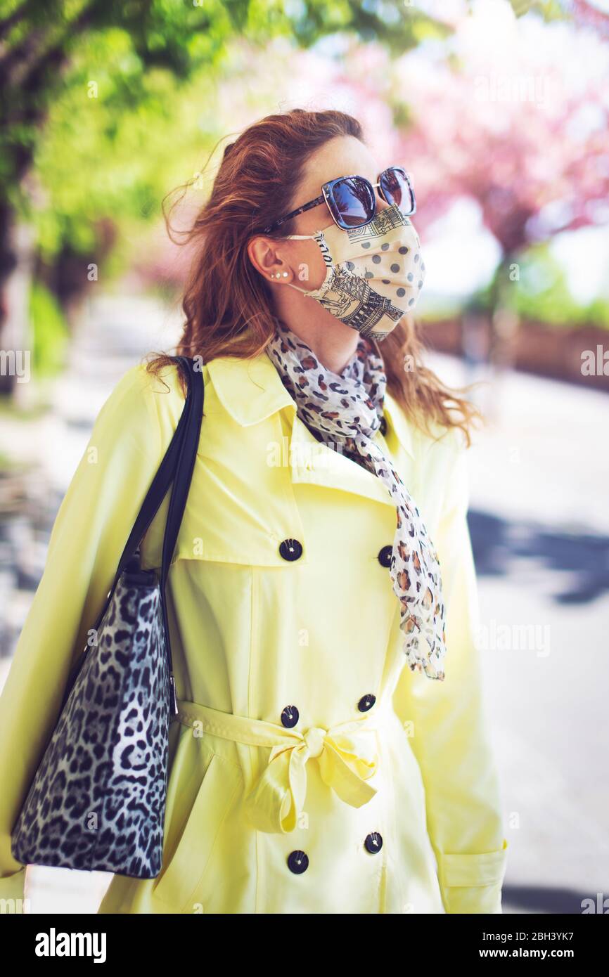 Junge Rotschopf Frau in gelben Mantel eine Sonnenbrille zu Fuß im Park während der Pandemie Stockfoto