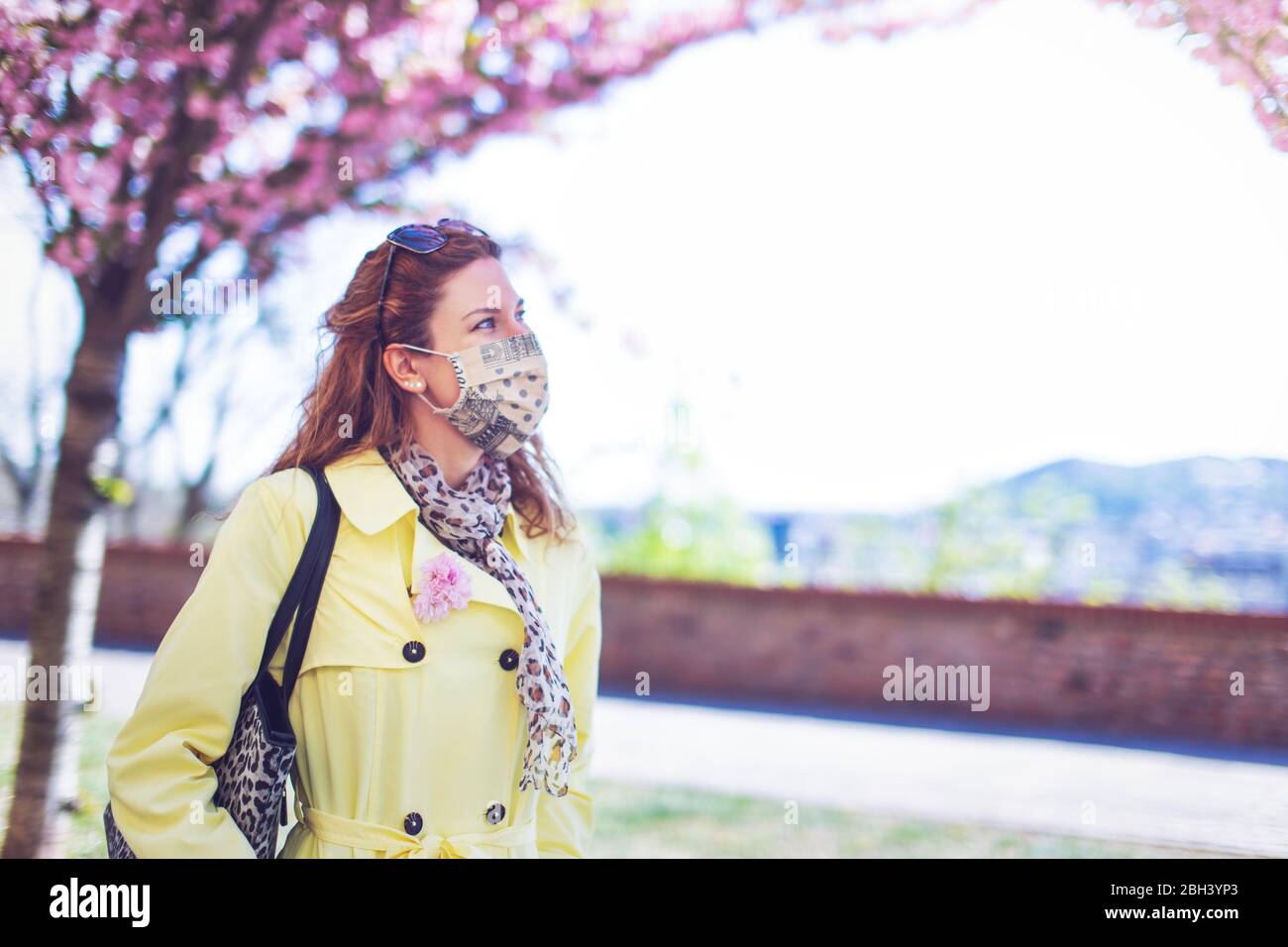 Junge Frau in Maske beim Spaziergang im Park während Sakura, Frühling Stockfoto