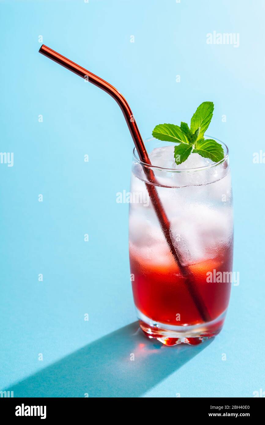 Ein Glas Wasser voller Eiswürfel, Mineralwasser und Erdbeersirup. Alkoholfreier Cocktail mit Erdbeersirup. Erdbeeren Limonade gesund Stockfoto