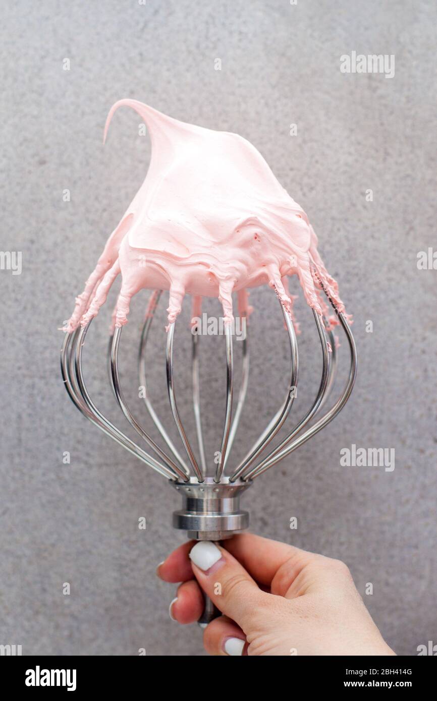 Rosa Schlagsahne schweizer Meringue auf dem großen Metallquirl. Schlichtes graues Hintergrundbild. Stockfoto