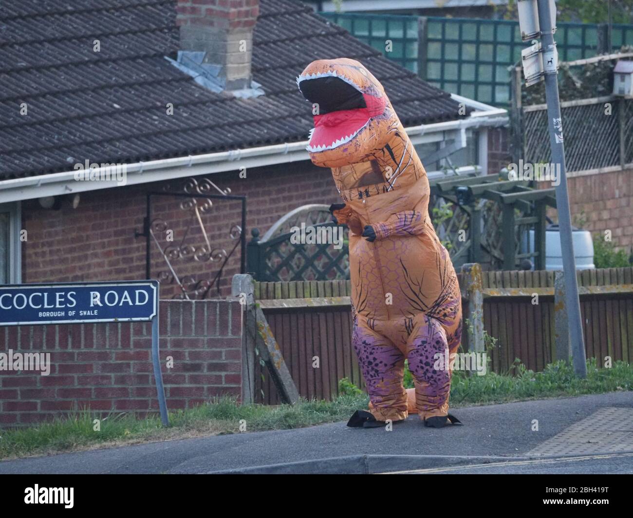 Minster on Sea, Kent, Großbritannien. April 2020. Eine Person in einem Dinosaurier-Kostüm klatscht für den NHS und kaufte sich heute Abend in Minster on Sea, Kent, ein Lächeln und einen Ruß von vorbeifahrenden Fahrern. Quelle: James Bell/Alamy Live News Stockfoto