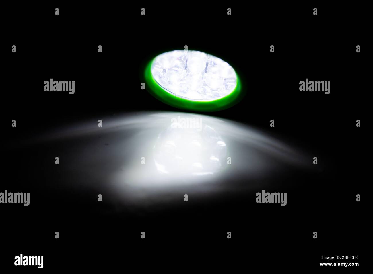 Grüne LED-Taschenlampe leuchtet auf einer weißen Oberfläche in einem abgedunkelten Raum Stockfoto