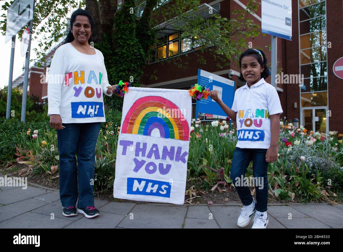 London, Großbritannien, 23. April 2020: Medizinische und unterstützende Mitarbeiter versammelten sich in der A&E Ambulance Bay im St George's Hospital, Tooting, um Clap für unsere Betreuer zu begleiten. Dieses 4-jährige Mädchen, Eden, hatte ein Regenbogenbanner gemacht und sie und ihre Mutter trugen selbstgemachte 'Thank You NHS' T-Shirts. Anna Watson/Alamy Live News Stockfoto