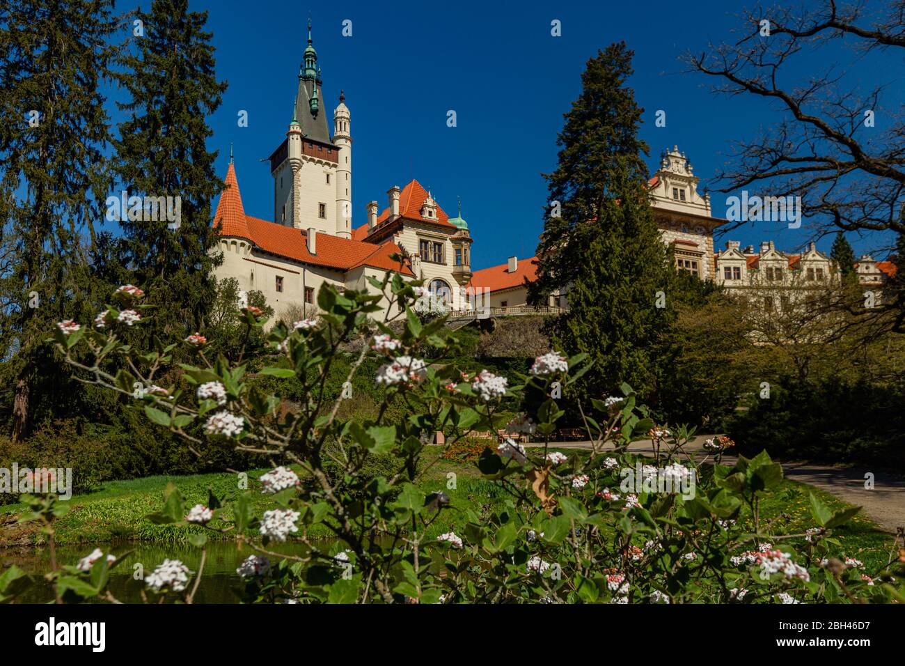 Pruhonice / Tschechische Republik - April 20 2020: Blick auf eine Burg, die am sonnigen Frühlingstag auf einem Hügel steht und einen strahlend blauen Himmel hat. Bush und weiße Blume Stockfoto