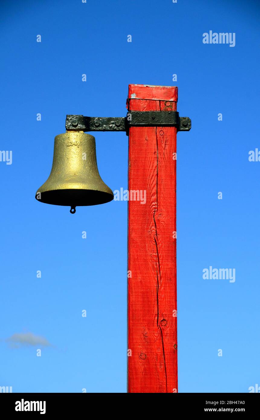 Eine Schiffswarnglocke, die auf einem roten hölzernen postat an einem Steg / Hafen montiert ist. Stockfoto
