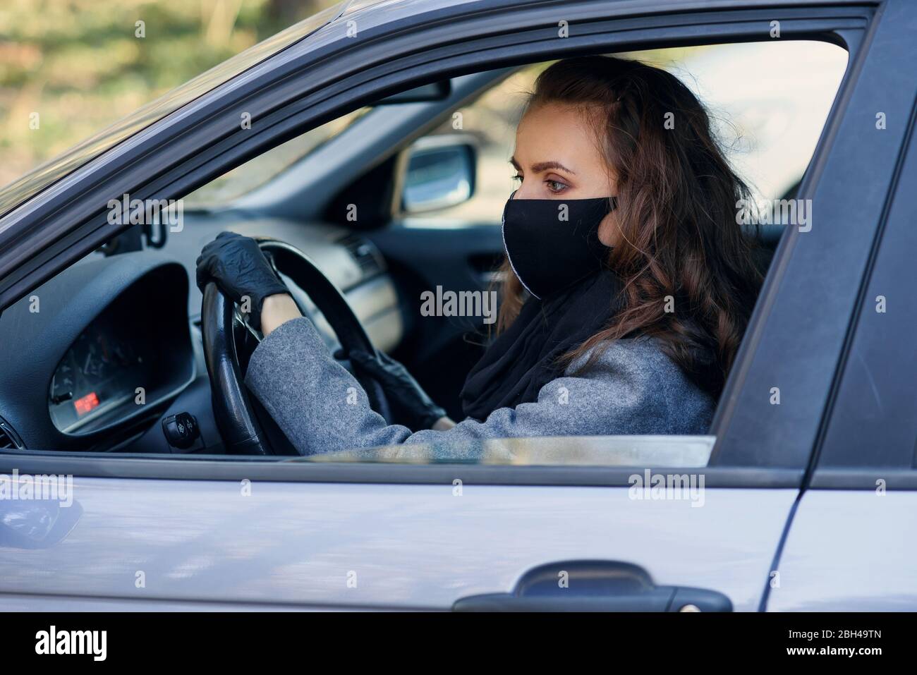 Geschäftsfrau in schützender Gesichtsmaske und Gummihandschuhen fährt ein Auto. Persönlicher Schutz während der Quarantäne. Weltpandemie des Coronavirus, persönliche PR Stockfoto