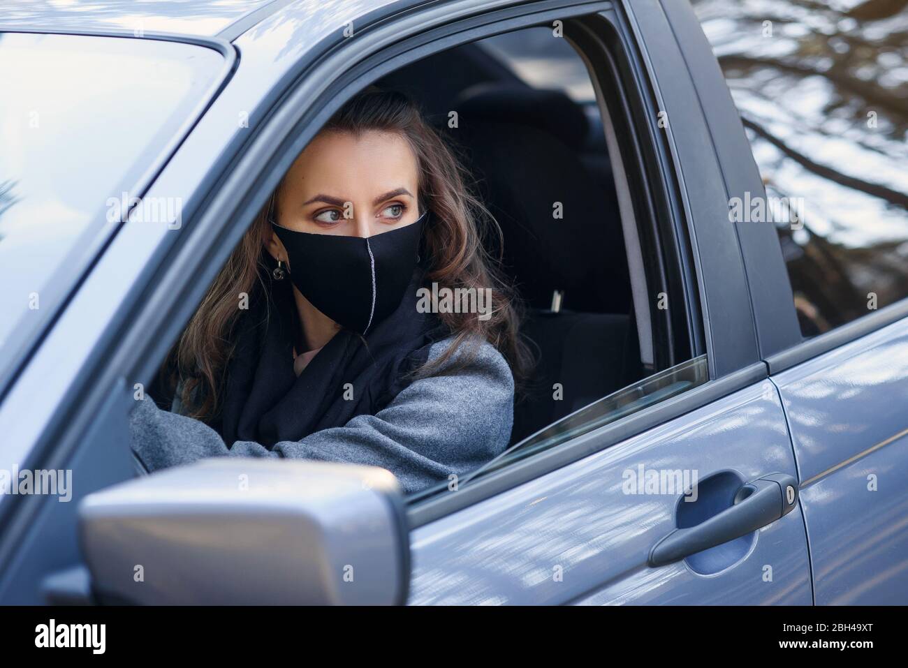 Geschäftsfrau in schützender Gesichtsmaske und Gummihandschuhen fährt ein Auto. Persönlicher Schutz während der Quarantäne. Weltpandemie des Coronavirus, persönliche PR Stockfoto