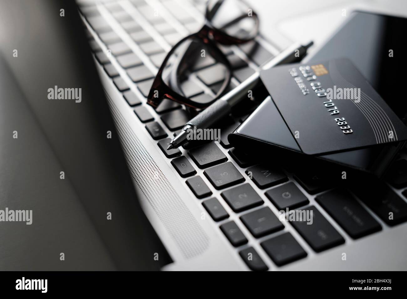 Kreditkarte, Smartphone, Stift und Brille auf Laptop-Tastatur Stockfoto