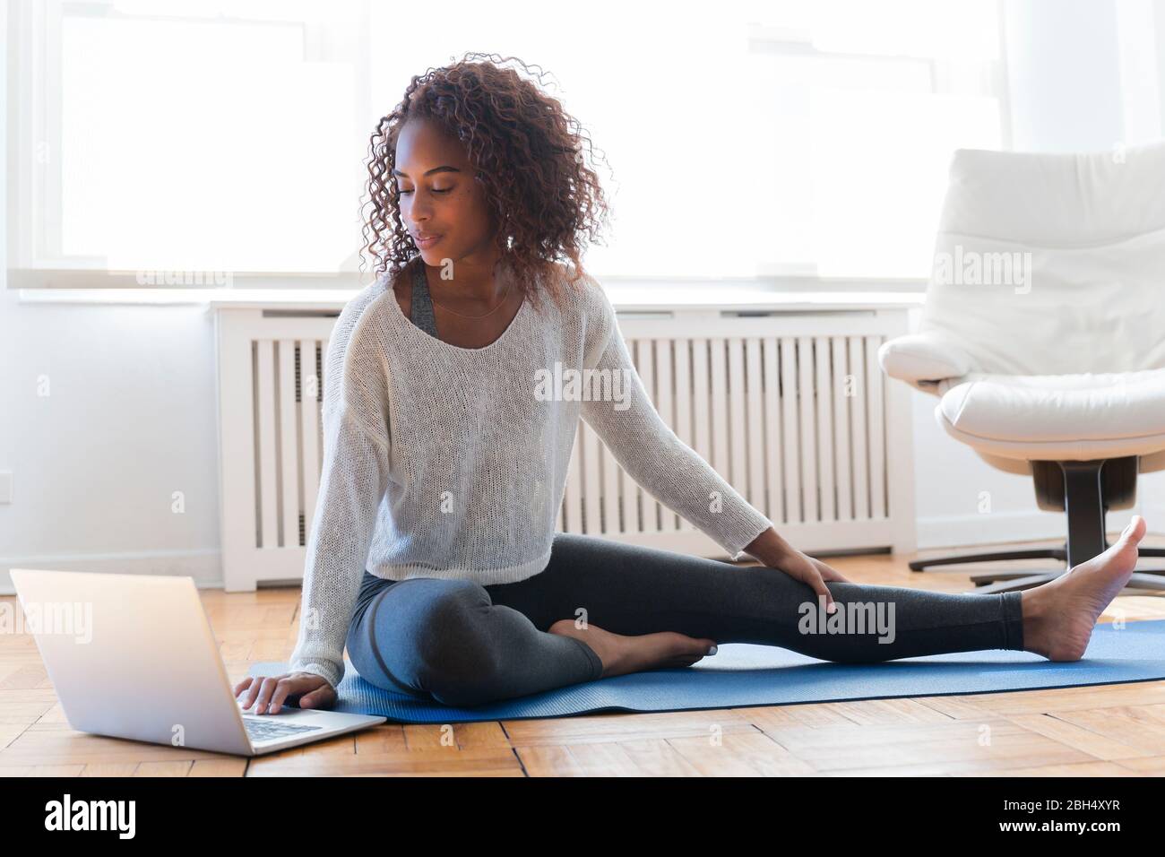 Frau mit Laptop auf Yoga-Matte Stockfoto