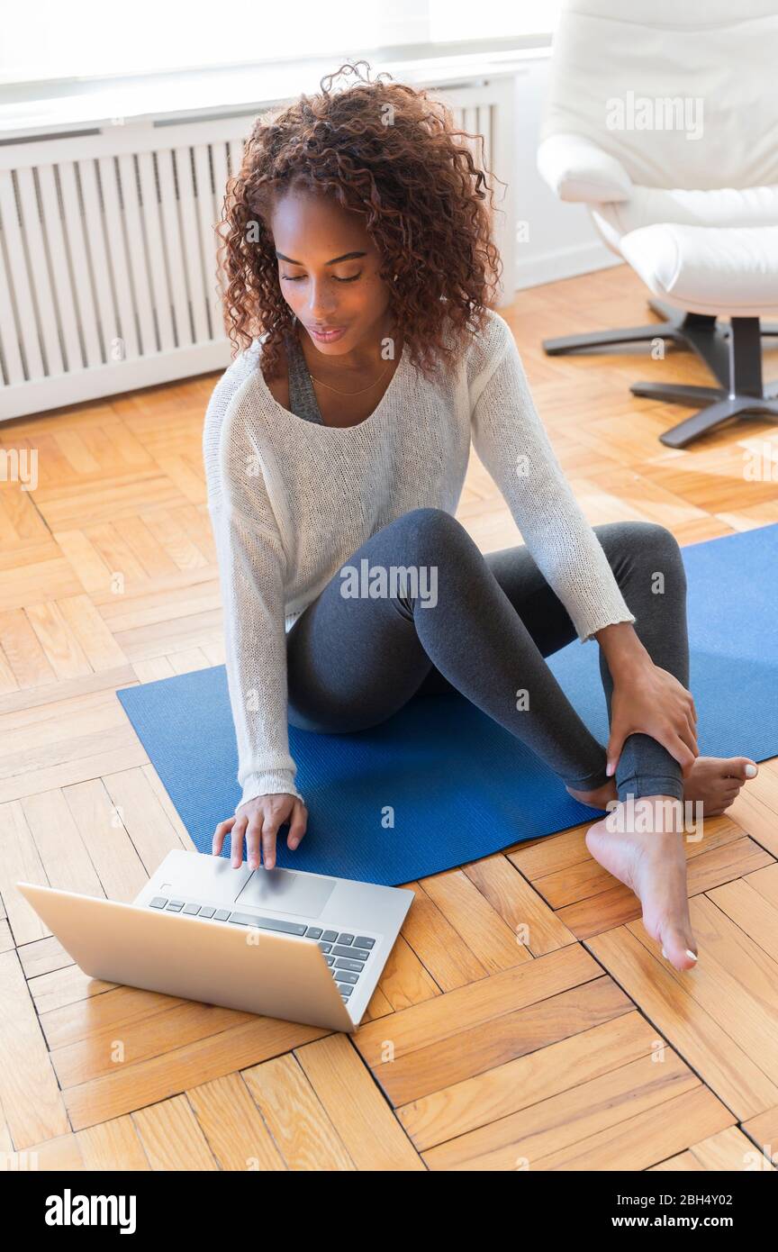 Frau mit Laptop auf Yoga-Matte Stockfoto