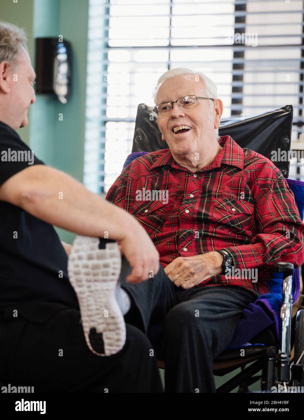 Krankenschwester mit lächelndem Fuß des älteren Mannes im Rollstuhl Stockfoto