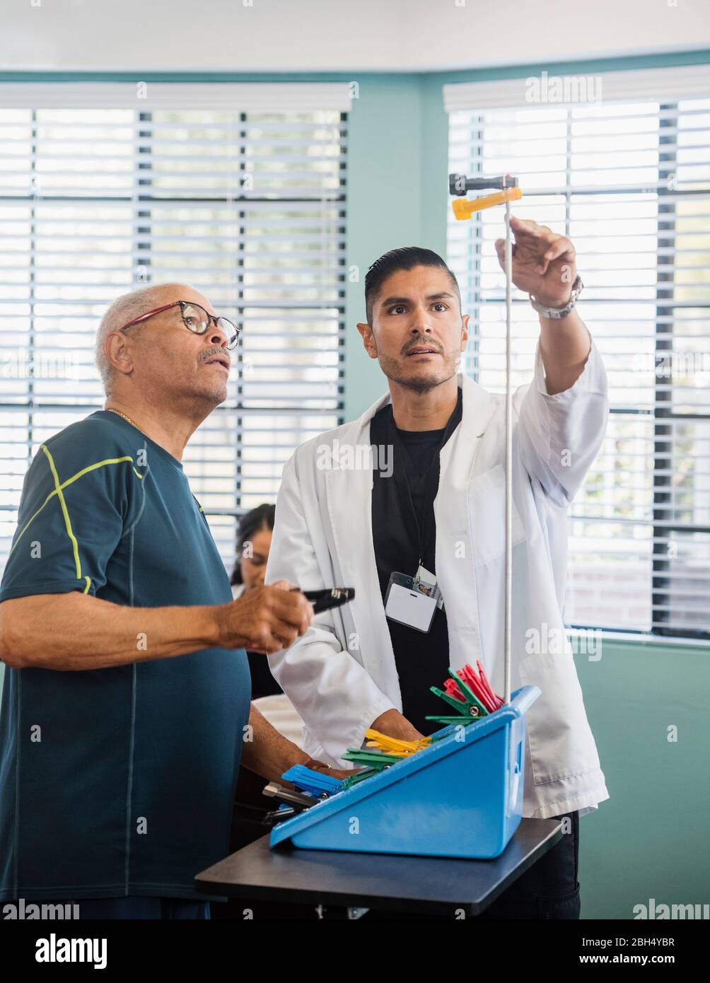 Arzt, der im Rehabilitationszentrum die Pflöcke eines älteren Mannes an der Stange zeigt Stockfoto