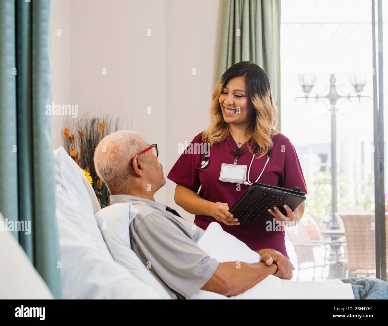 Lächelnde Krankenschwester hält Zwischenablage von älteren Mann im Bett Stockfoto