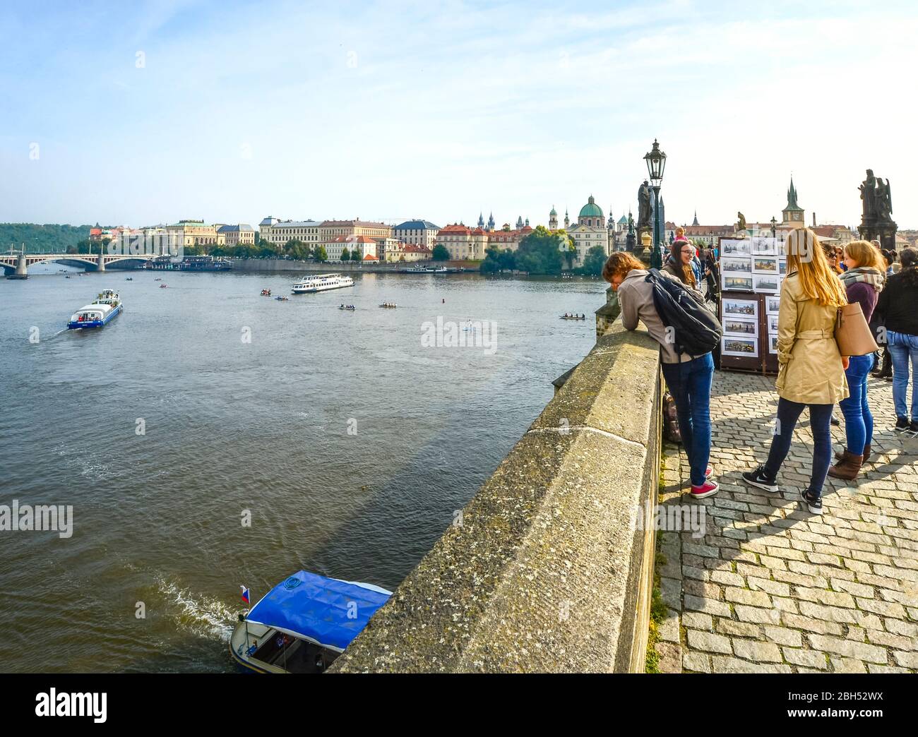 Eine Gruppe junger Tschechen unterhalten sich auf der Karlsbrücke mit Blick auf die Moldau und der Altstadt in der Ferne in Prag, Tschechien. Stockfoto