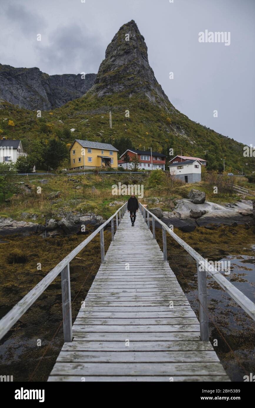 Mann, der auf einer Brücke durch eine Klippe auf den Lofoten, Norwegen, läuft Stockfoto