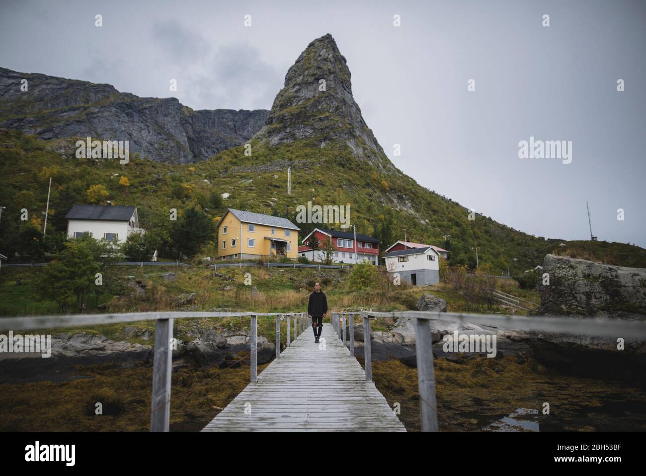 Mann, der auf einer Brücke durch eine Klippe auf den Lofoten, Norwegen, läuft Stockfoto