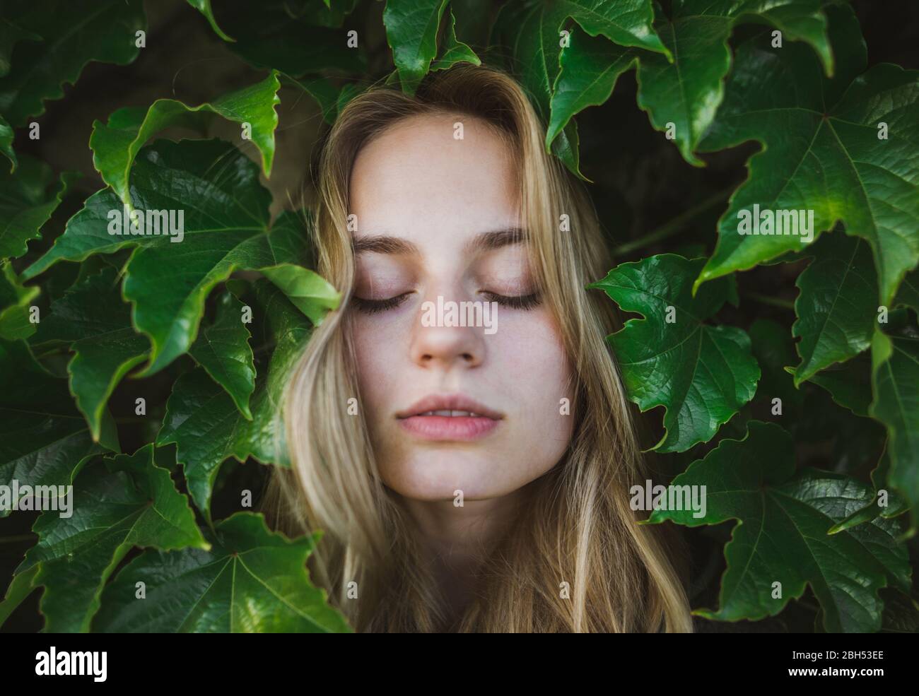 Frau mit geschlossenen Augen zwischen Blättern Stockfoto