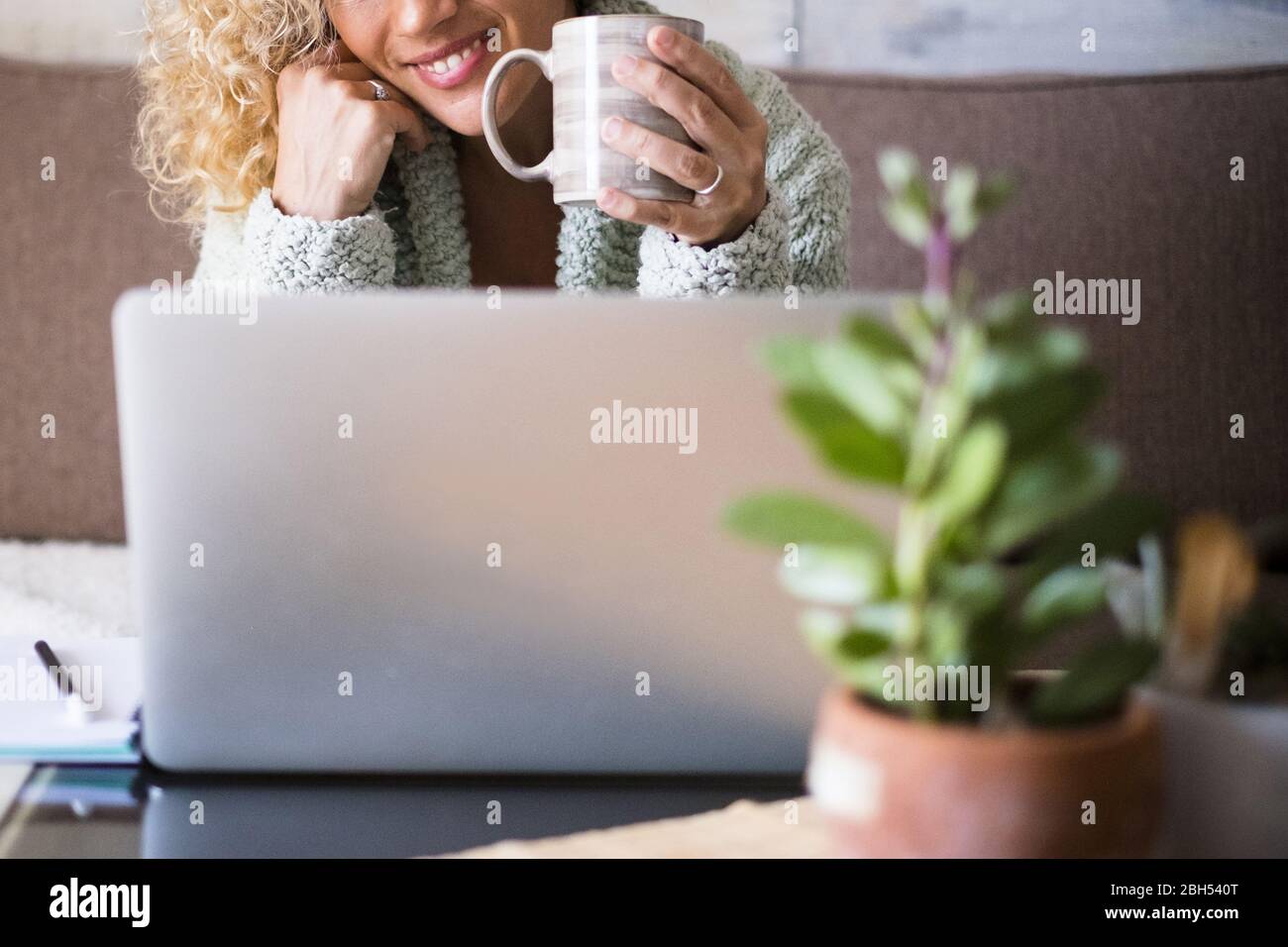 Lächelnde Frau hält Getränk hinter dem Laptop Stockfoto