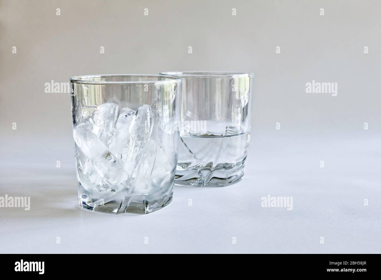 Profilansicht von Trinkgläsern aus Eis und Wasser (geschmolzenes Eis) in transparenten Gläsern auf neutralem Hintergrund, Begriffe von Zeit und Veränderung, Farbe Stockfoto