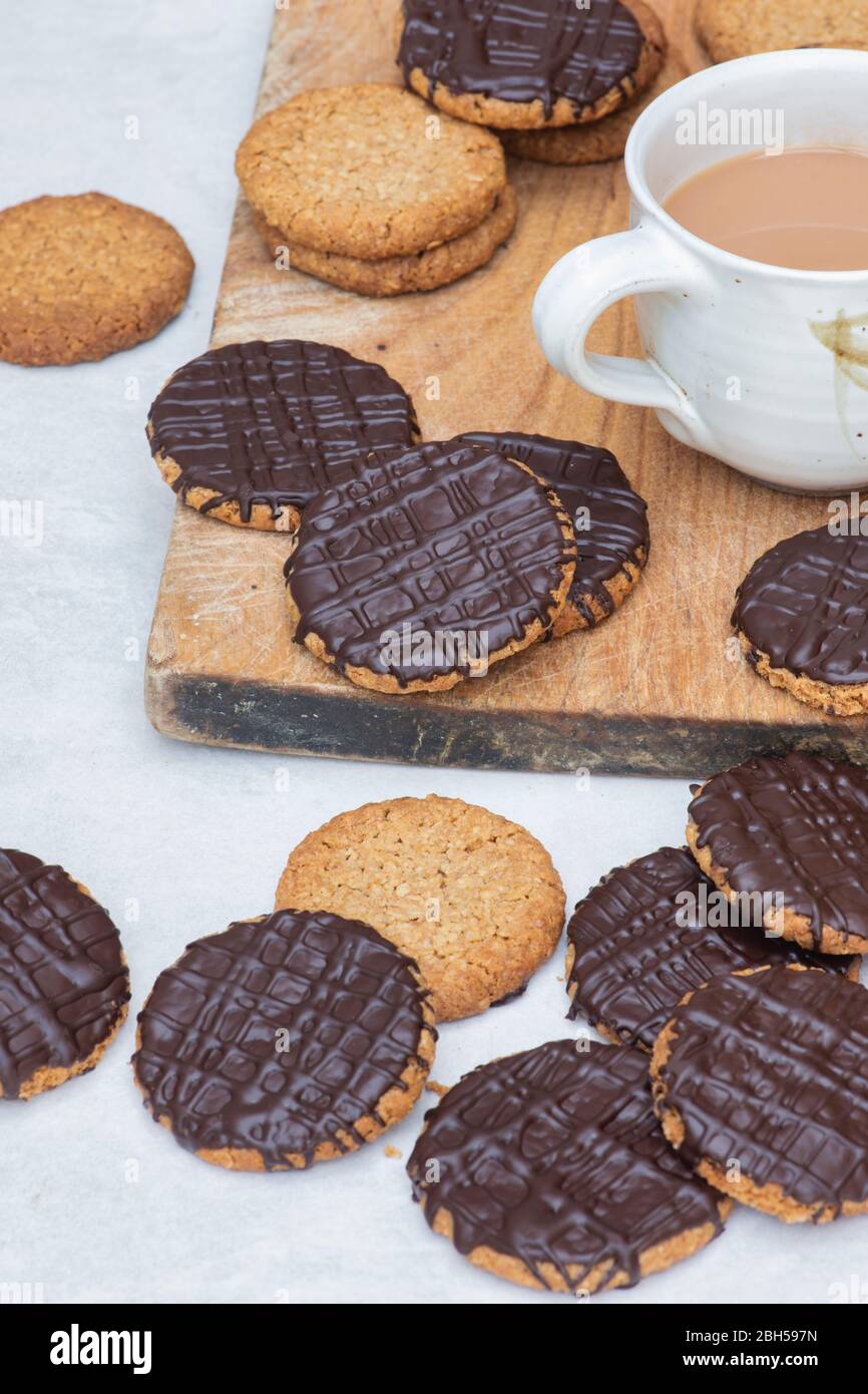 Hausgemachte, mit dunkler Schokolade überzogene Hobnob-Kekse auf einem Holzbrett mit einer Tasse Tee Stockfoto