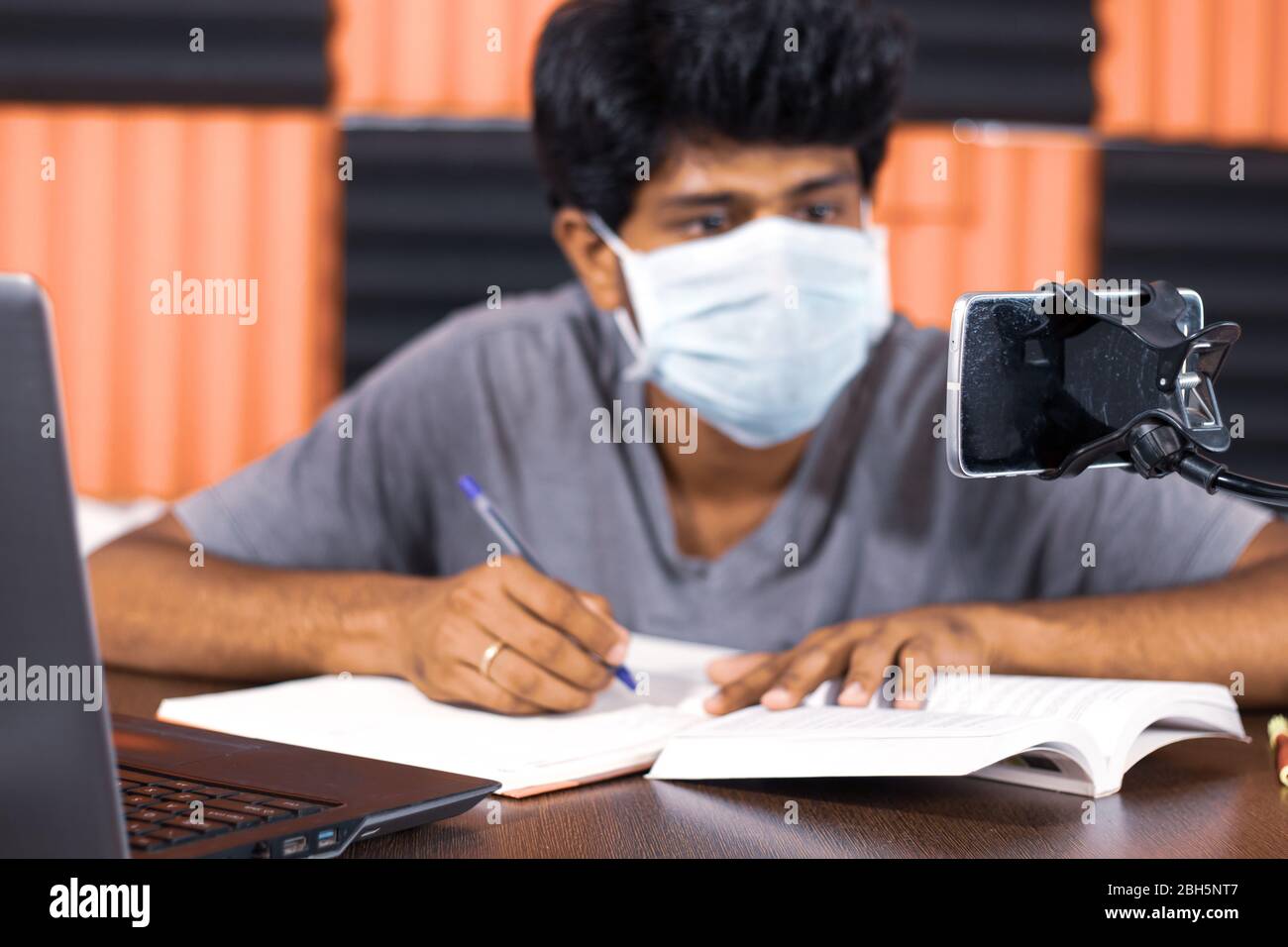 Junger Mann mit medizinischer Maske E-Learning zu Hause durch covid-19 oder Coronavirus Isolation Konzept - College-Student Notizen durch den Blick in virtuelle Stockfoto