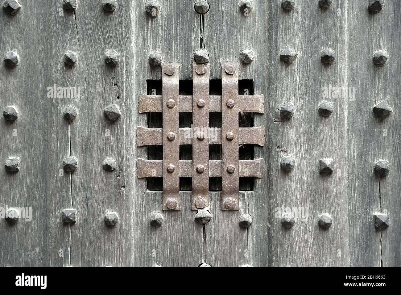 Ansicht Fenster Schlitz mit Schutz rostigen Metallstreifen Kreuz und quer auf alten hölzernen Tür-Panel mit Reihen von Holzperlen besetzt. Stockfoto