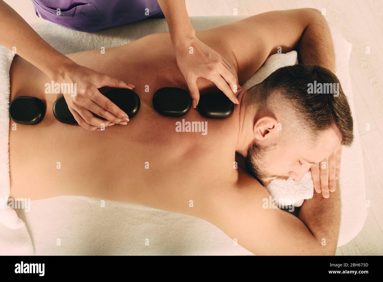 Der hübsche Mann im Spa Resort erhält eine Massage mit heißen Steinen. Spezialmassage mit glatten, beheizten Steinen Stockfoto