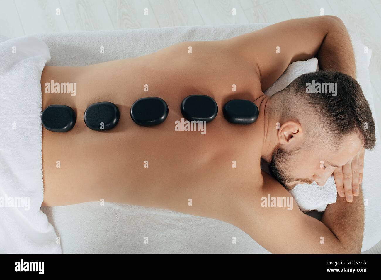 Entspannende Hot Stone Massage. Blick von oben schöner Mann mit Stein auf dem Rücken. Spa und Resor Stockfoto