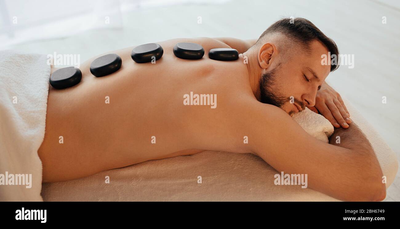 Der hübsche Mann im Spa Resort erhält eine Massage mit heißen Steinen. Spezialmassage mit glatten, beheizten Steinen Stockfoto