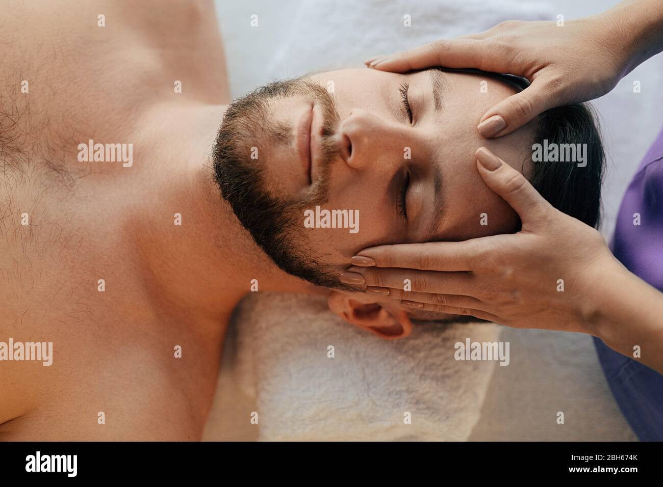 Schöner Mann, der sich bei einer Kopfmassage im Wellnessresort mit geschlossenen Augen entspannt. Massagekopfschmerzbehandlung Stockfoto