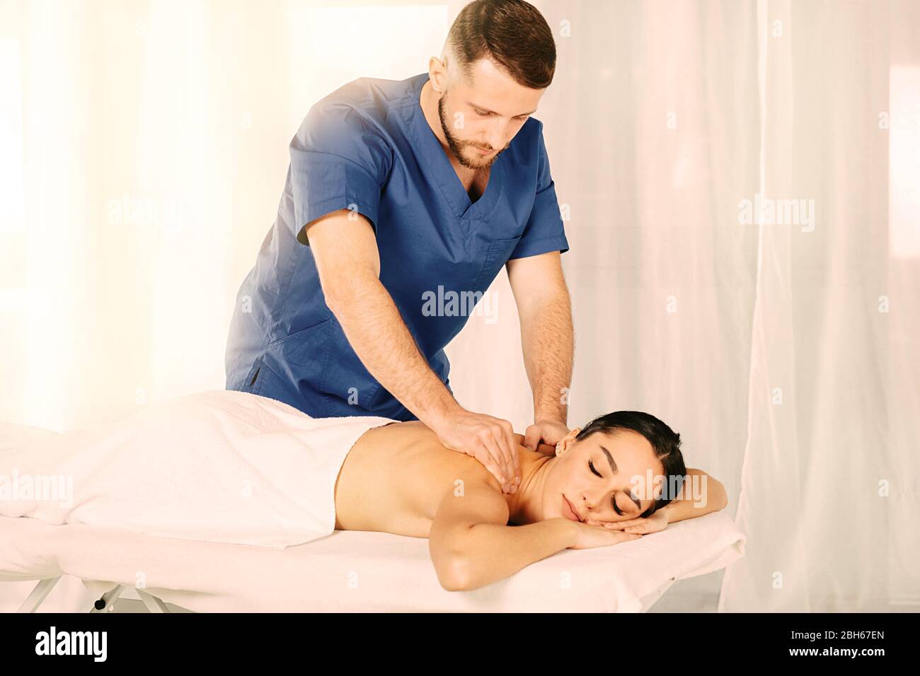 Sonnige Entspannungsmassage. Handsome Massage Therapeut tun Rückenmassage zu einer schönen Frau Stockfoto