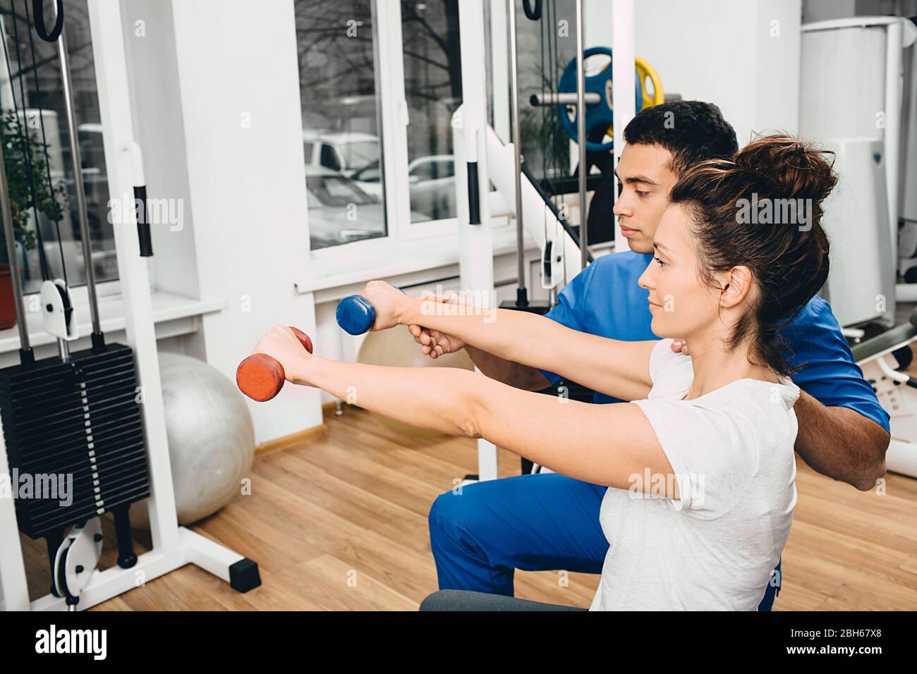 Der Trainer im Fitnessstudio hilft einer Frau, Übungen durchzuführen. Übungen mit Kurzhanteln zur Stärkung der Muskeln der Hände Stockfoto