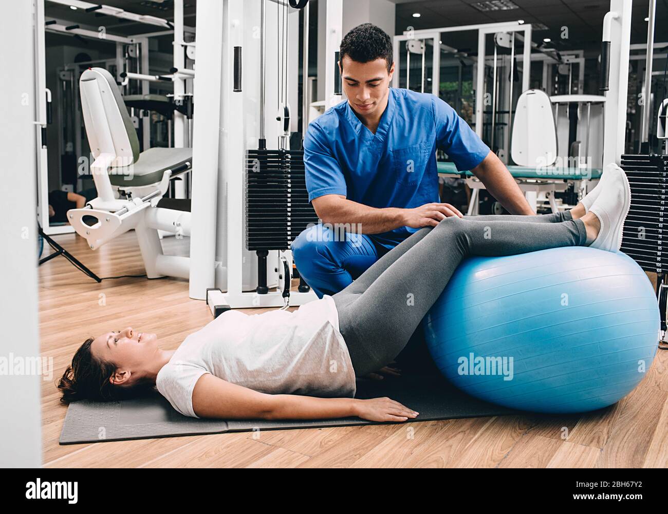 Physiotherapeut hält einen Fitnessball, der dem Patienten hilft, Übungen für den unteren Rücken zu machen. Schmerzen im unteren Rücken. Gesundheitsturnsport Stockfoto